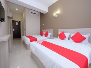 A hotel room with two beds, each with white bedding and red accents, a desk, a door, and an air conditioning unit.