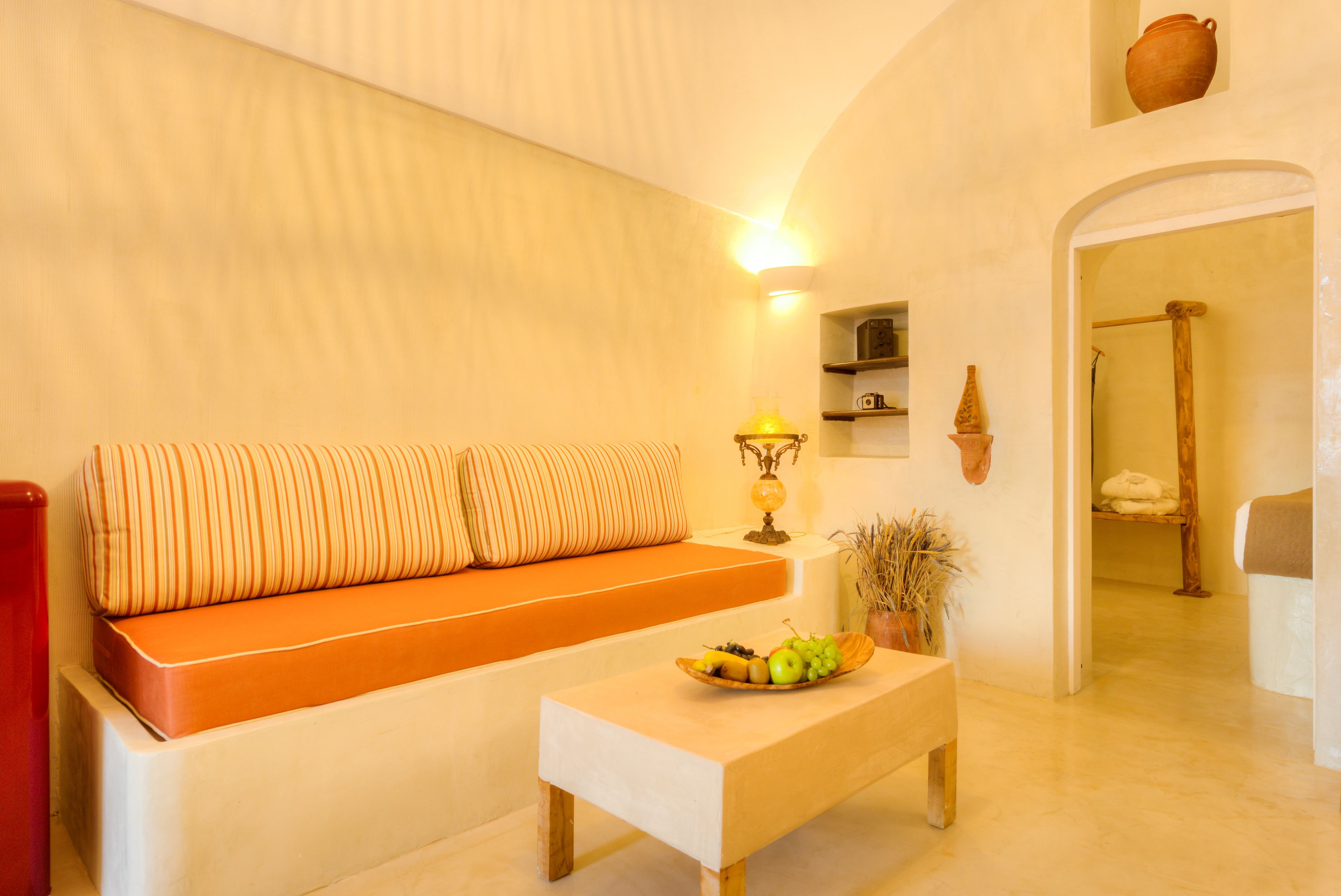 Una sala de estar acogedora con un sofá, una mesa de centro de madera con fruta, y un estante en la pared con adornos.