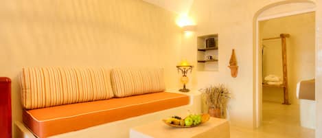 Una sala de estar acogedora con un sofá, una mesa de centro de madera con fruta, y un estante en la pared con adornos.