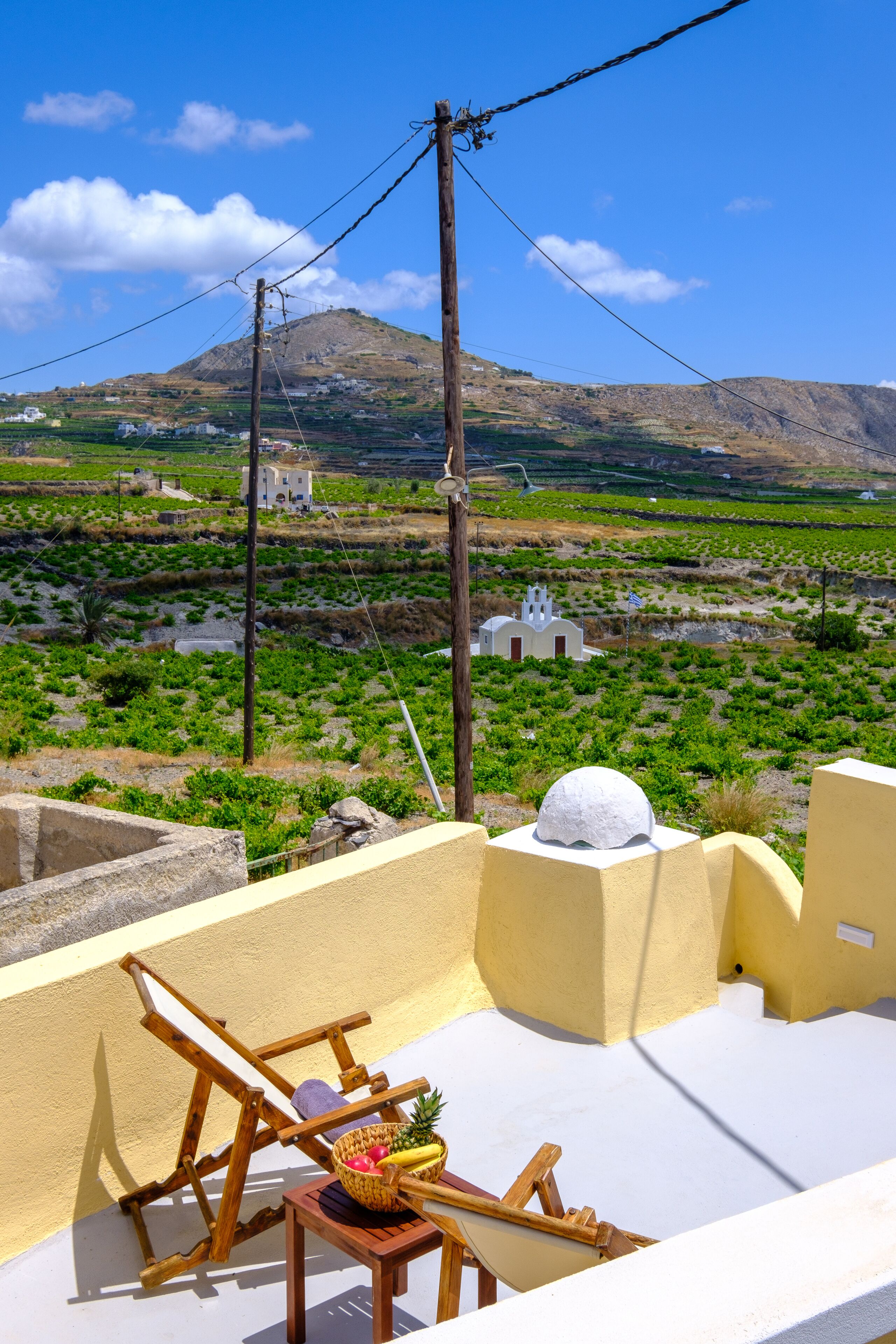 A terrace with a view of a rural landscape, including fields and a small church.