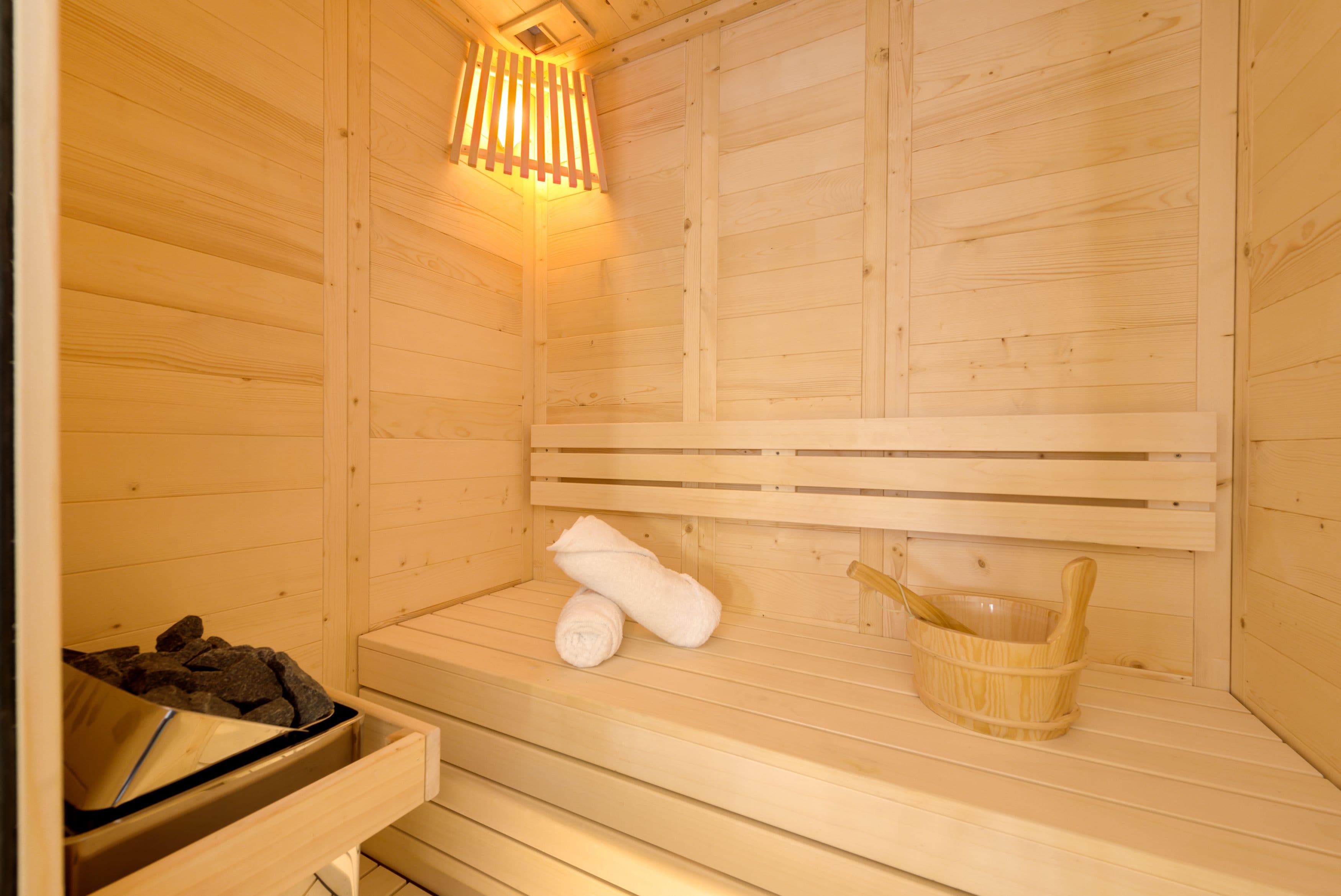 A wooden sauna with a bench, a towel, and a wooden bucket.