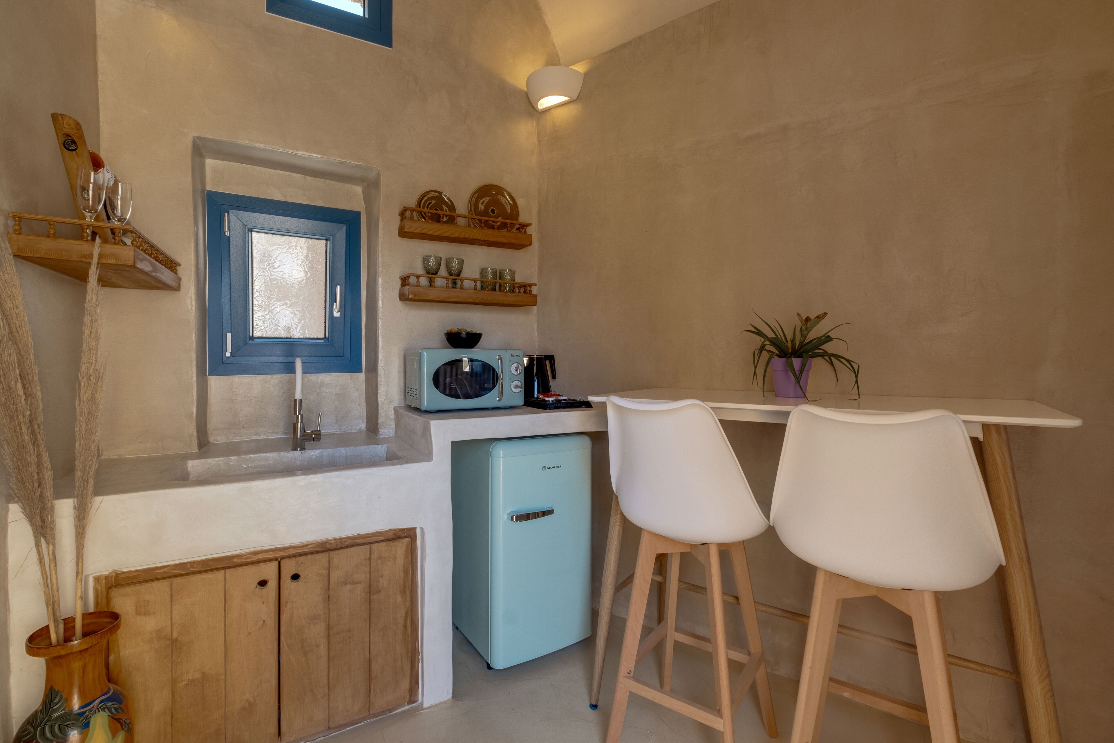 Eine kleine Küche mit einem blauen Kühlschrank, Holzschränken, einer weißen Arbeitsplatte und zwei weißen Barhocker.
