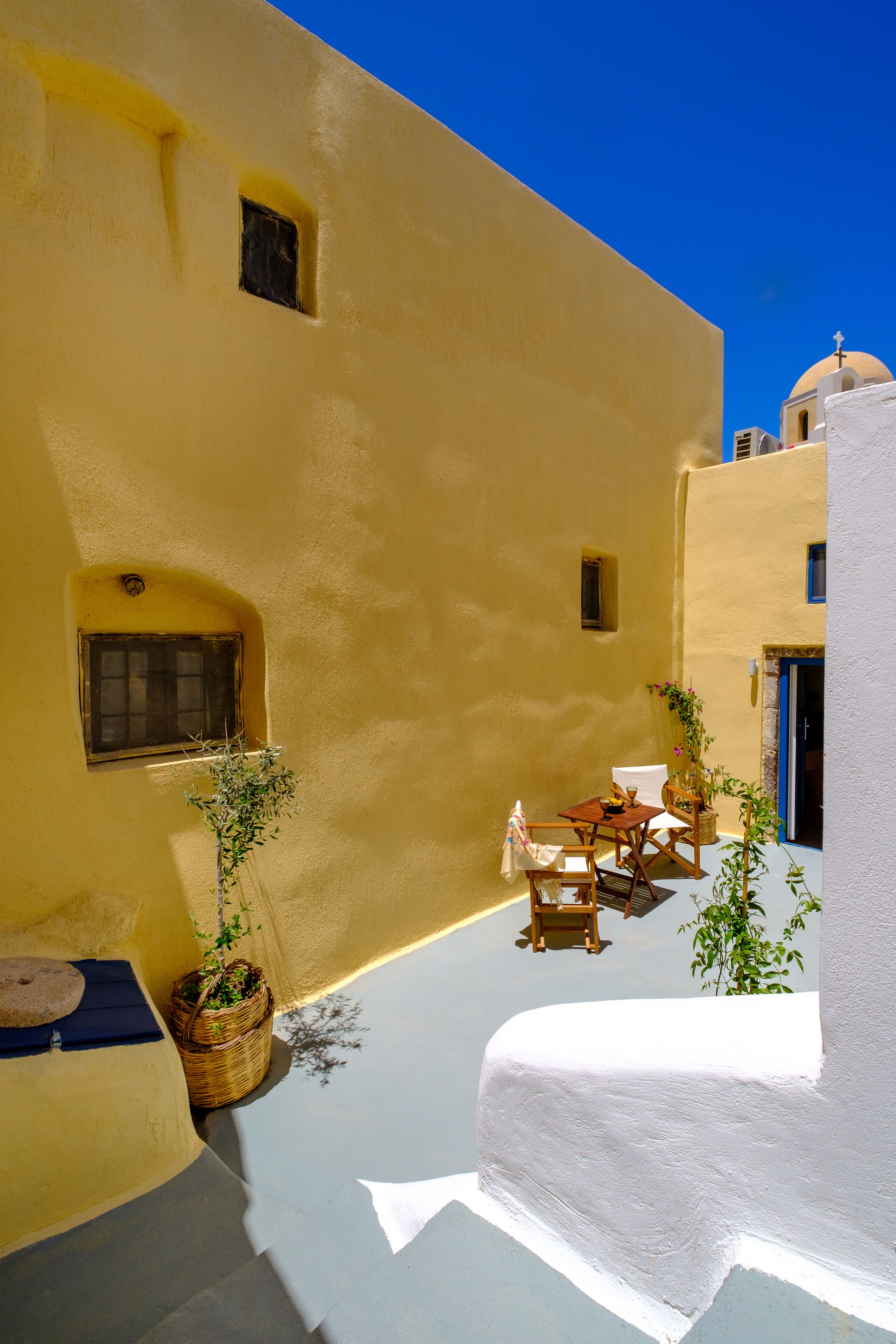 A sunlit courtyard with a white table and chairs, a small window, and a basket with plants.