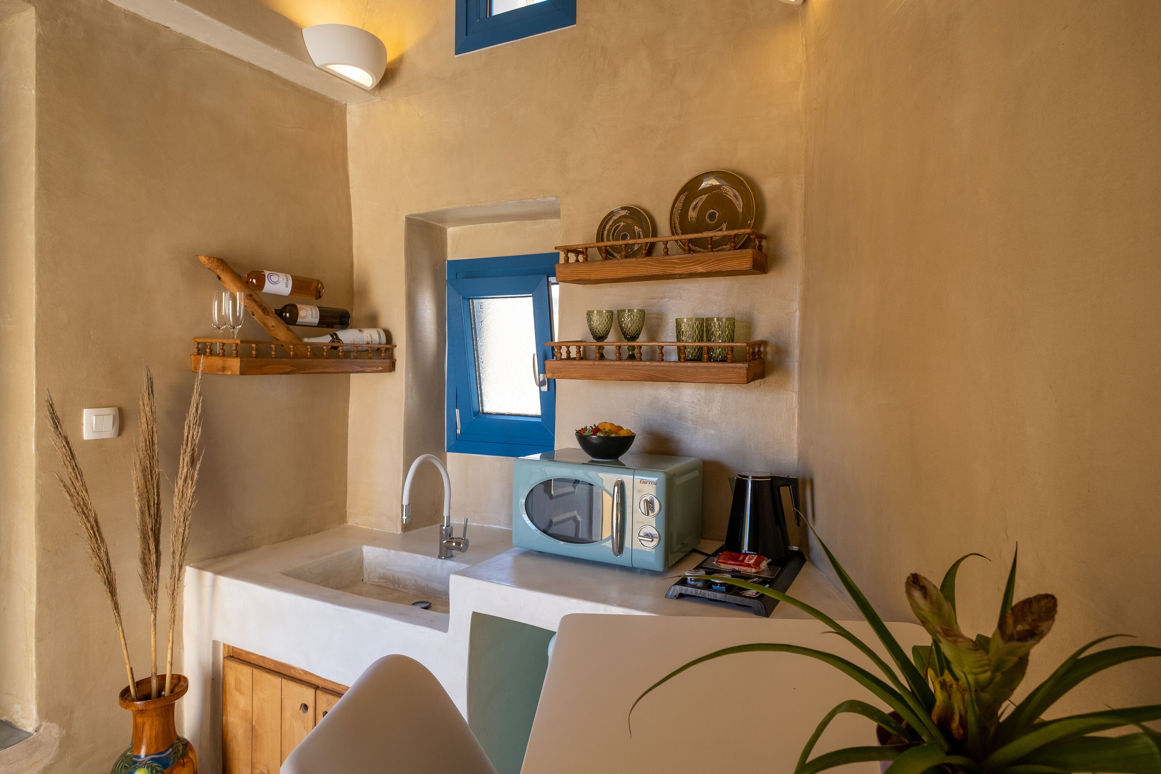 Una cocina compacta con microondas, lavamanos y estantes de madera arriba.
