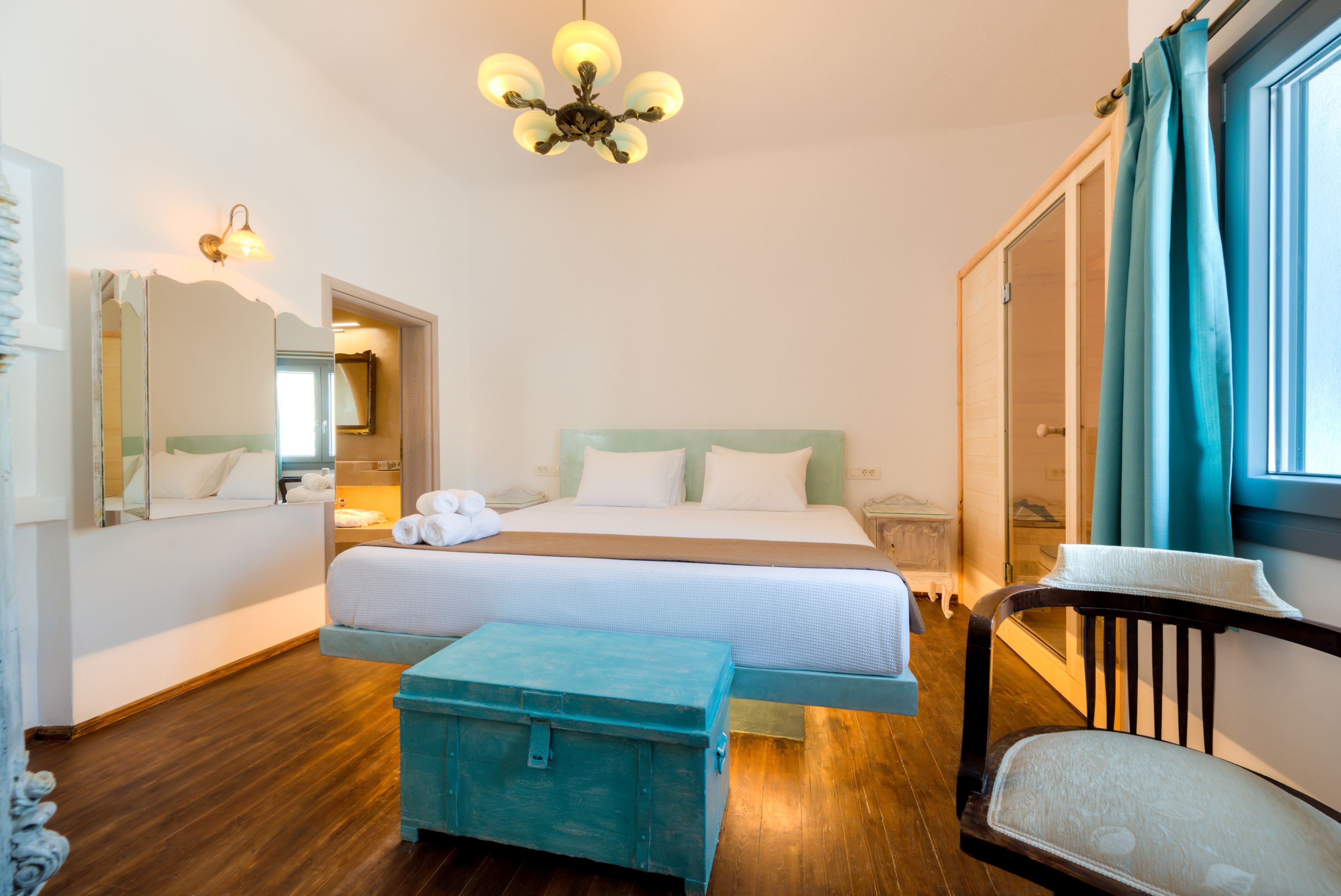 A hotel room with a large bed, a chest of drawers, a wooden bench, a nightstand, and a mirror.
