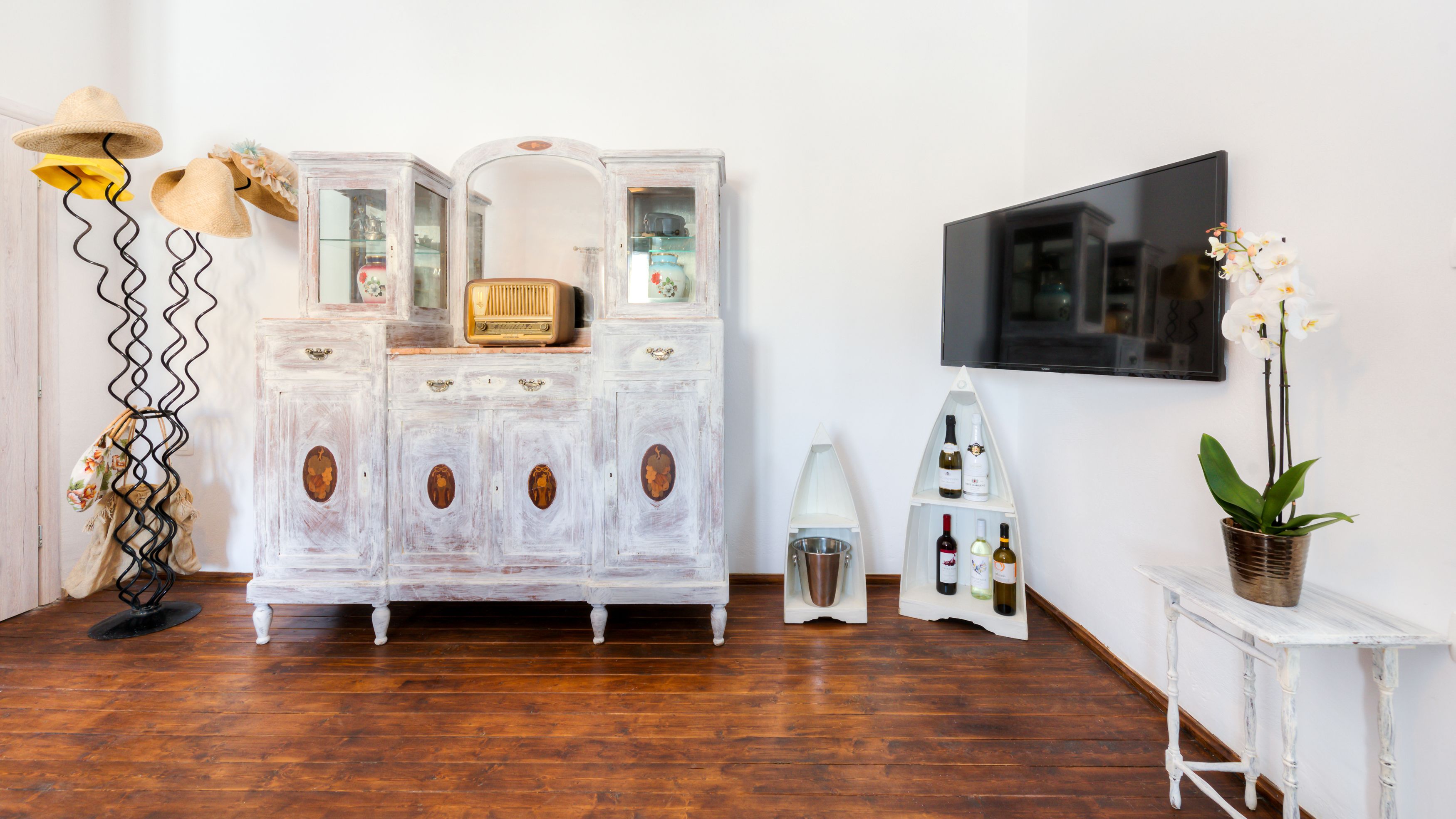 A room with a vintage white cabinet, a television mounted on the wall, and a potted orchid on a small table.