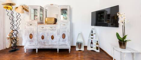 A room with a vintage white cabinet, a television mounted on the wall, and a potted orchid on a small table.