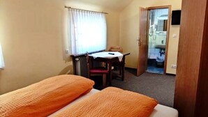 A small hotel room with two beds, a table, a chair, and a bathroom visible through an open door. - Double room without balcony 10 - Gasthaus Zum Pälterwald (Oberzent)