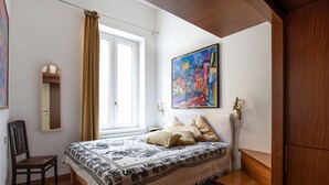 Una camera da letto con un letto, una sedia, una finestra con tende, un quadro e un armadio in legno.