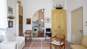 Un soggiorno con un divano bianco, una sedia di legno, una televisione e un mobile in legno con un modellino di nave.