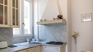 Una cucina con mobili bianchi, un piano di lavoro in marmo, un fornello a gas e una finestra.