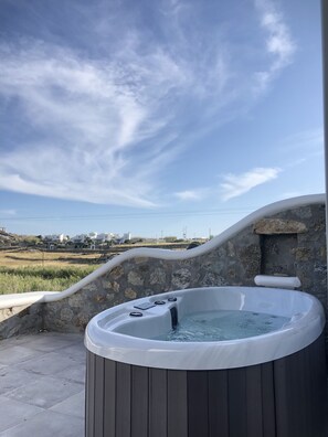 Banheira de hidromassagem com parede de pedra ao fundo e vista para casas distantes.