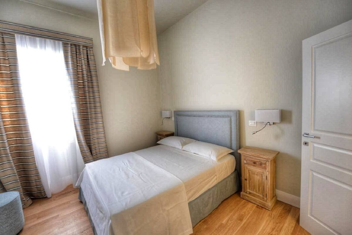 Une chambre à coucher avec un lit, des rideaux, une table de chevet et une commode, ainsi qu’une porte.