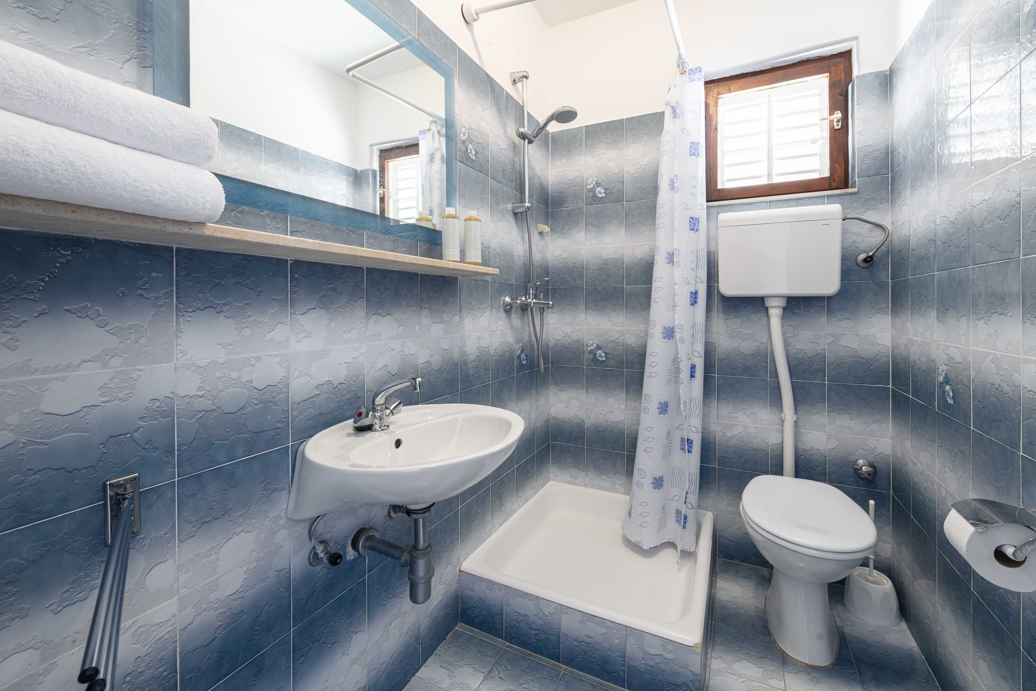 Een badkamer met een wastafel, toilet, douche en een raam.