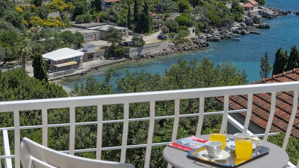 Ein Balkon mit Frühstückstisch, mit Blick auf eine Küstenstadt mit Gebäuden und einer felsigen Küstenlinie.