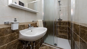 Ein modernes Badezimmer mit einer Duschkabine, einem weißen Waschbecken und einer Wand mit Marmorplatten.