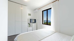 Ein Schlafzimmer mit Bett, Kleiderschrank, Schreibtisch, Fernseher und einem Fenster mit Blick ins Freie.