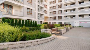 A multi-story residential building with balconies, a landscaped garden area with a bench, and a paved walkway.