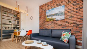 A modern living room with a brick wall, a sofa, a dining area, and a bookshelf.