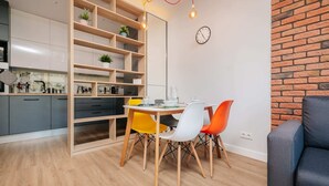 A modern kitchen with wooden shelves, a dining table with colorful chairs, and a brick accent wall.