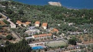 An aerial view of a coastal residential area with houses, a swimming pool, and a road curving along the coastline. - Villaggio Turistico Defensola (Vieste)