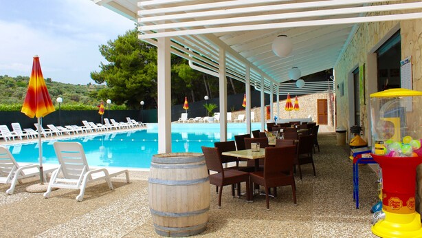 A poolside area with lounge chairs, a dining area, and a children's play area. - Villaggio Turistico Defensola (Vieste)