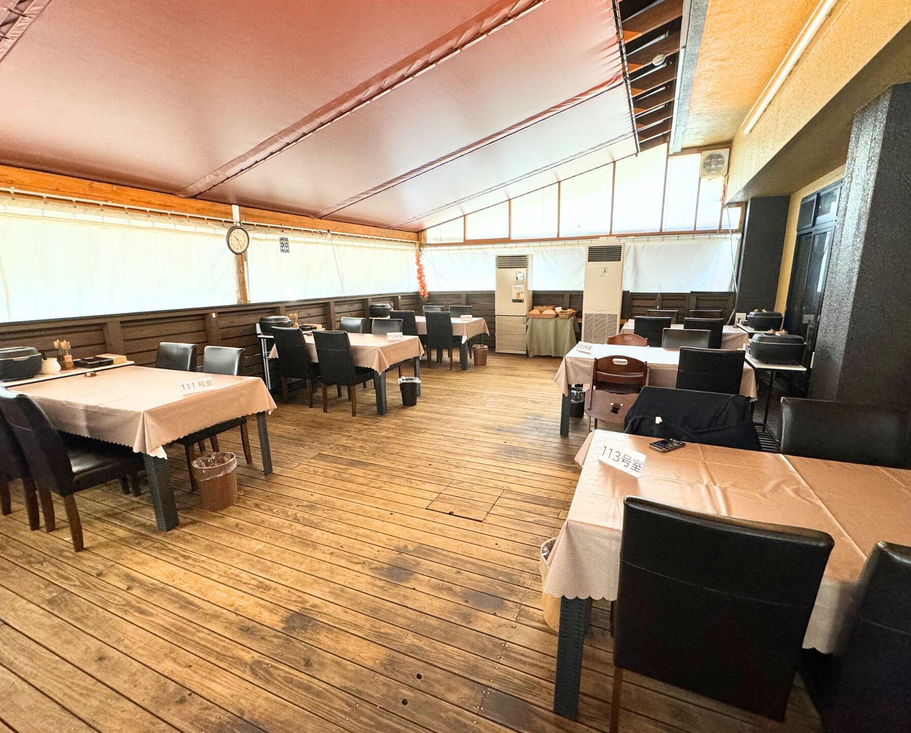 A restaurant with wooden flooring, tables with numbered placemats, and a large tented roof.
