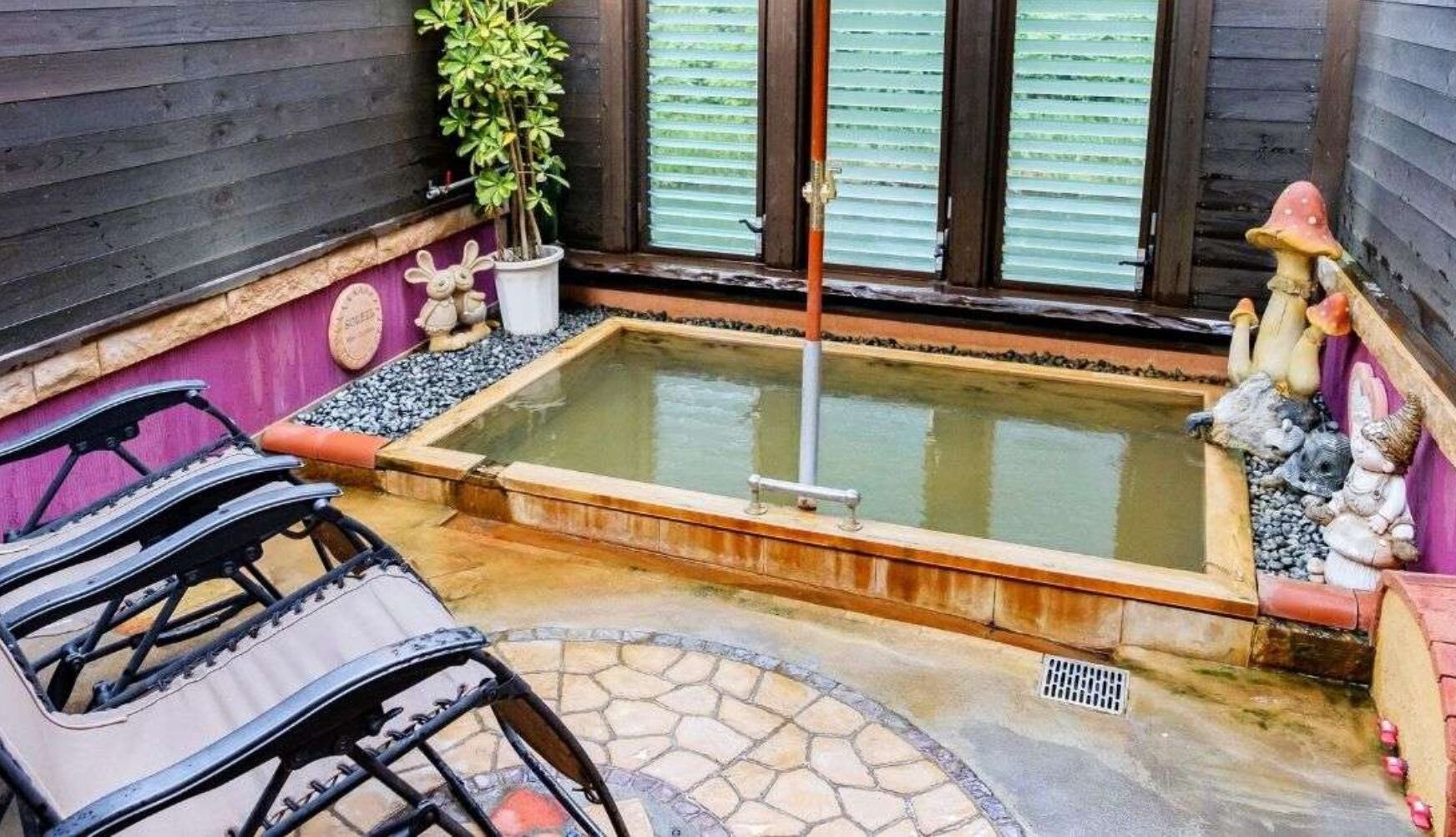 A hot tub with a wooden border, surrounded by a stone patio, a small table, and chairs.