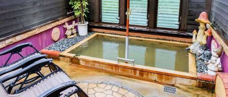 A hot tub with a wooden border, surrounded by a stone patio, a small table, and chairs.