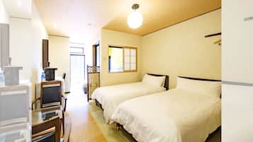 A hotel room with two beds, a desk with a chair, a small table, and a window.