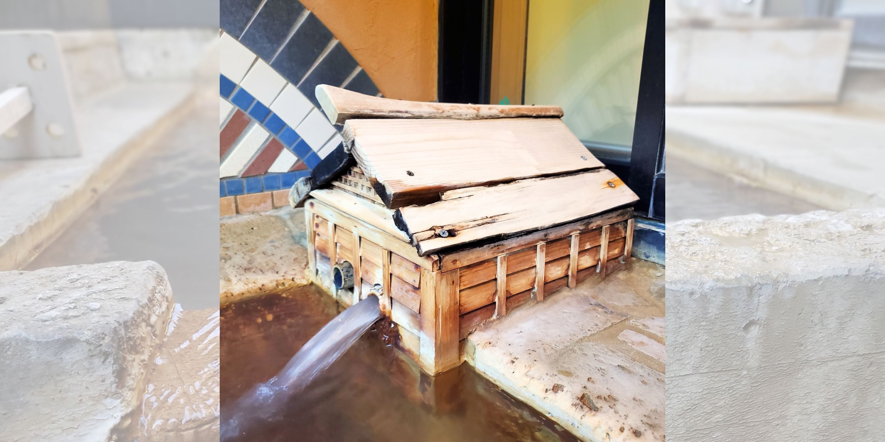 A wooden structure with a metal pipe discharging water into a pool.