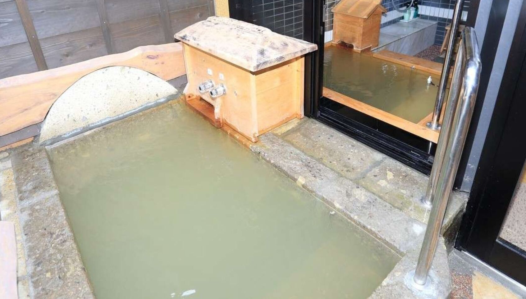 Ett traditionellt japanskt onsen-bad med ett träbadkar och en plattform av sten.