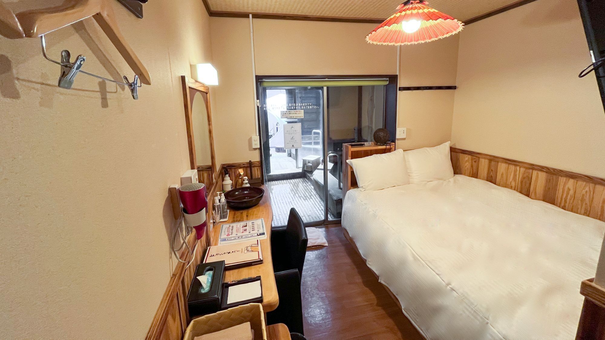 A hotel room with a bed, a desk with a mirror, a hairdryer, and a window.