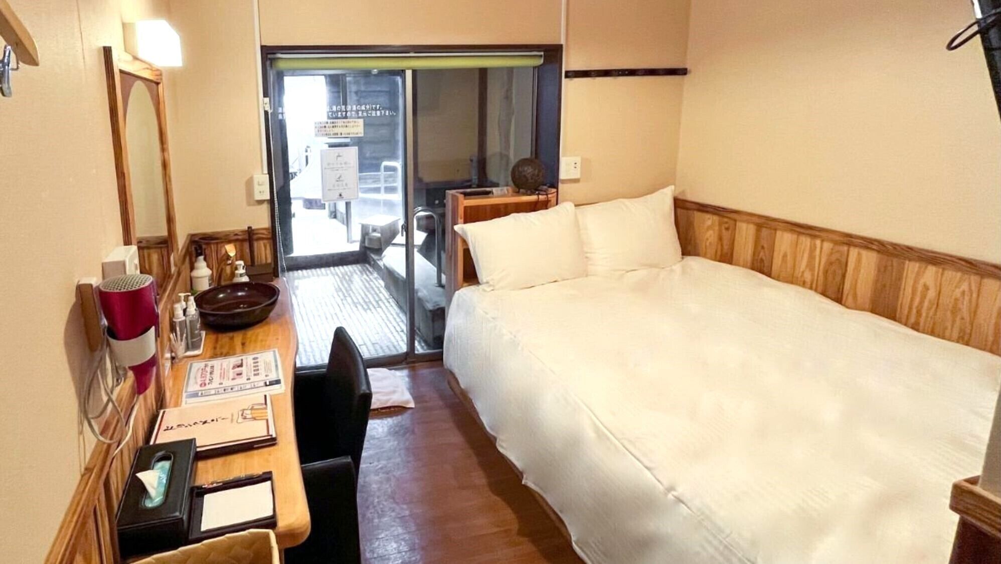 A hotel room with a bed, a desk with a mirror, a hairdryer, and a window.