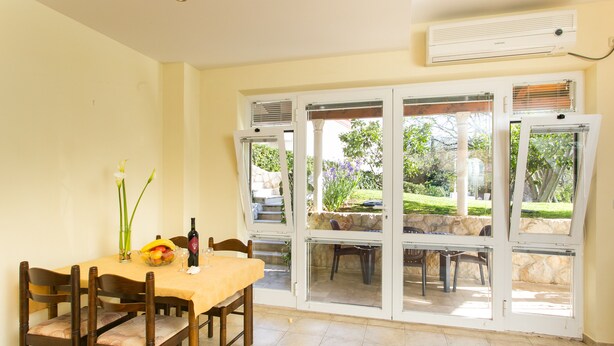 A dining area with a table set for four, a vase with flowers, and a bottle of wine. - Apartments Radic (Dubrovnik)