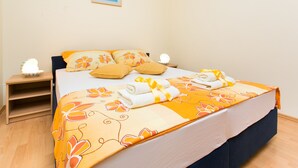 A neatly made bed with floral bedding, a bedside table with a lamp, and a framed picture on the wall. - Apartments Radic (Dubrovnik)