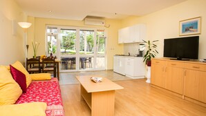 A living room with a sofa, coffee table, and a TV. There is a dining area with chairs and a table. The room has wooden flooring and white cabinets. - Apartments Radic (Dubrovnik)