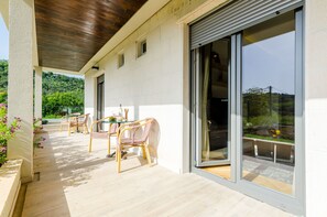 Ein überdachter Außenbereich mit Tisch und Stühlen, einer Glasschiebetür und Blick ins Grüne.