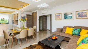 A modern living room with a brown sofa, yellow cushions, a dining area with a table and chairs, and a chandelier. - Villa Dolores Apartments  (Dubrovnik)