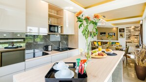 A modern kitchen with a central island, a microwave, and a sink. There is a dining area with a sofa and a table set for a meal. - Villa Dolores Apartments  (Dubrovnik)