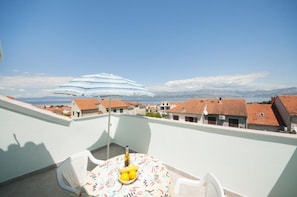 A balcony with a table, chairs, and a striped umbrella. - Apartments Jasenka Supetar (Supetar)
