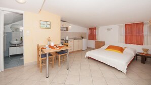 Ett kompakt hotellrum med ett litet kök, en matplats och en säng med orange sängkläder.