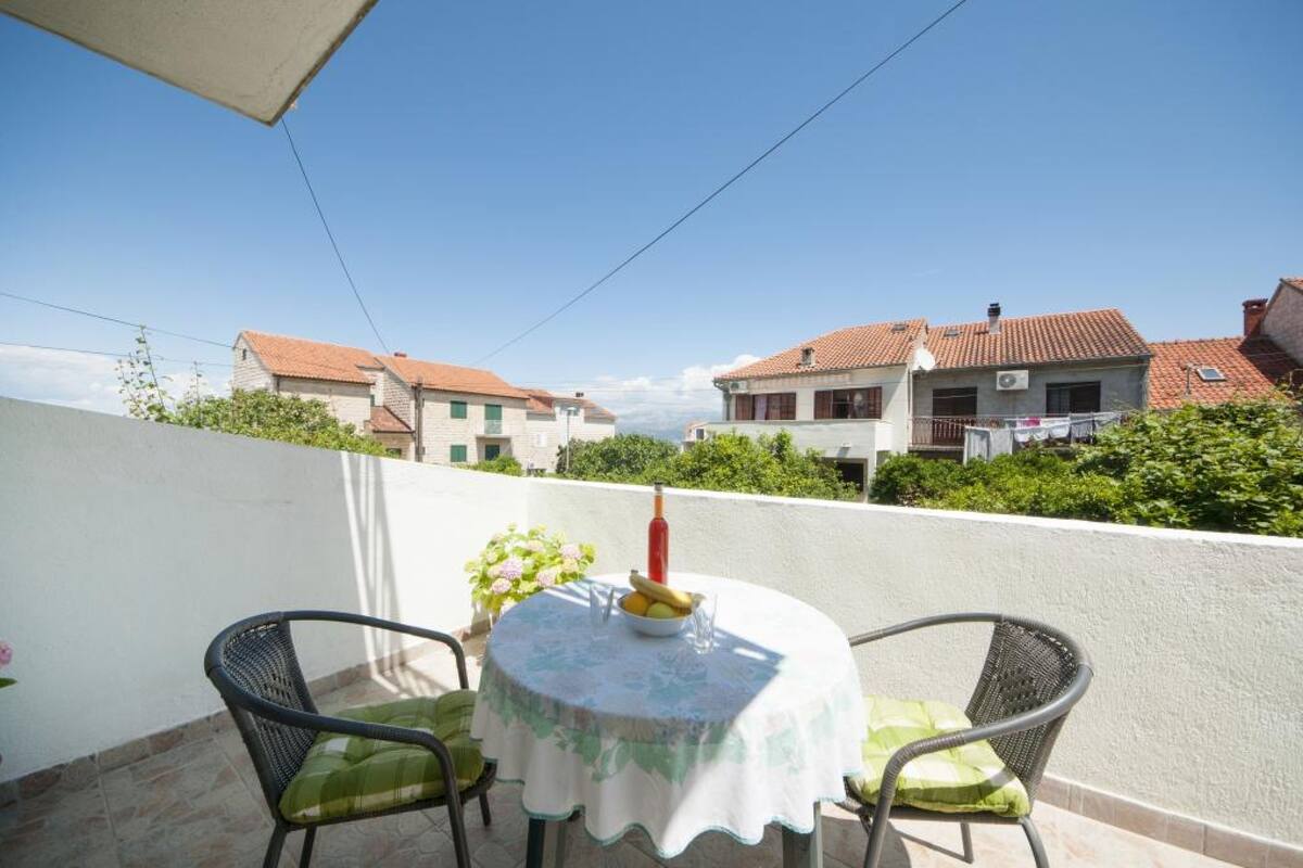 A balcony with a table set for two, a bottle, and a bowl of fruit.