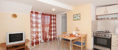 A compact living space with a kitchenette, a dining area with a table and chairs, a television, and a patterned curtain.