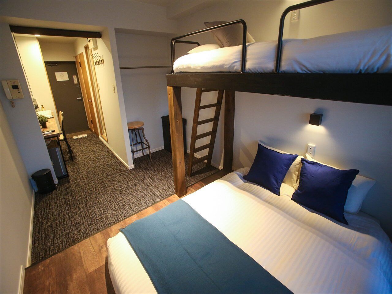A bunk bed room with a desk and chair, a ladder, and a small stool.