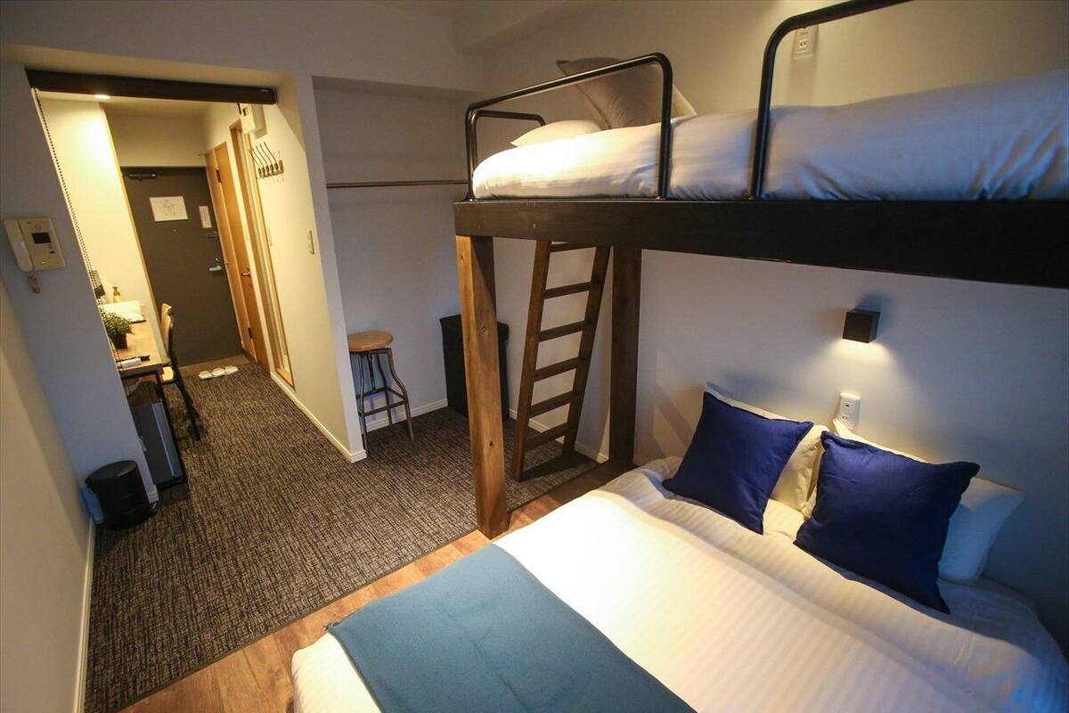 Une chambre avec un lit superposé, un bureau et une chaise, une échelle et un petit tabouret.