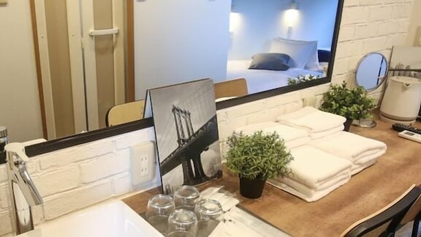A hotel bathroom with a white brick wall, a large mirror, a sink, a towel rack, a small potted plant, and a framed picture on the counter. - TABIGOYA LIFE＆TRIP HAKATA EAST (Fukuoka)