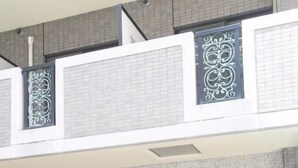 A building entrance with a tiled facade, a metal gate, and a glass door leading inside. - TABIGOYA LIFE＆TRIP HAKATA EAST (Fukuoka)