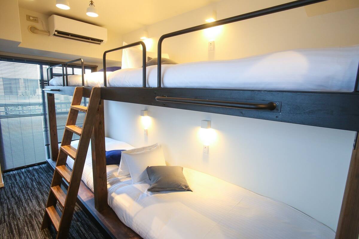 Une chambre avec un lit superposé, une échelle, des lampes de chevet et un appareil de climatisation.