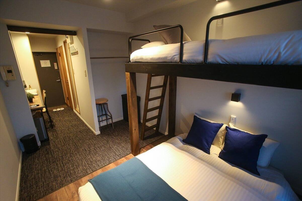 Une chambre avec un lit superposé, un bureau et une chaise, une échelle et un petit coin salle de bain.